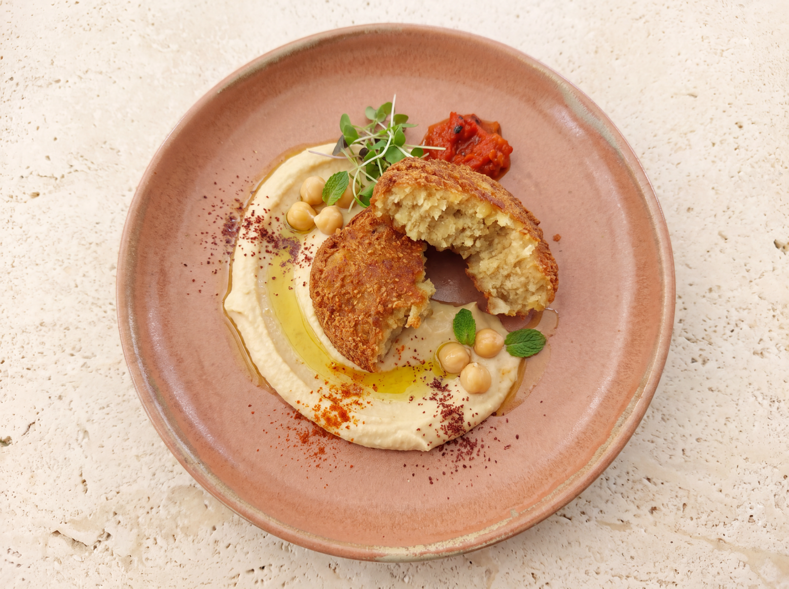 Falafels ouverts au centre d’une assiette terracotta, servis sur du houmous